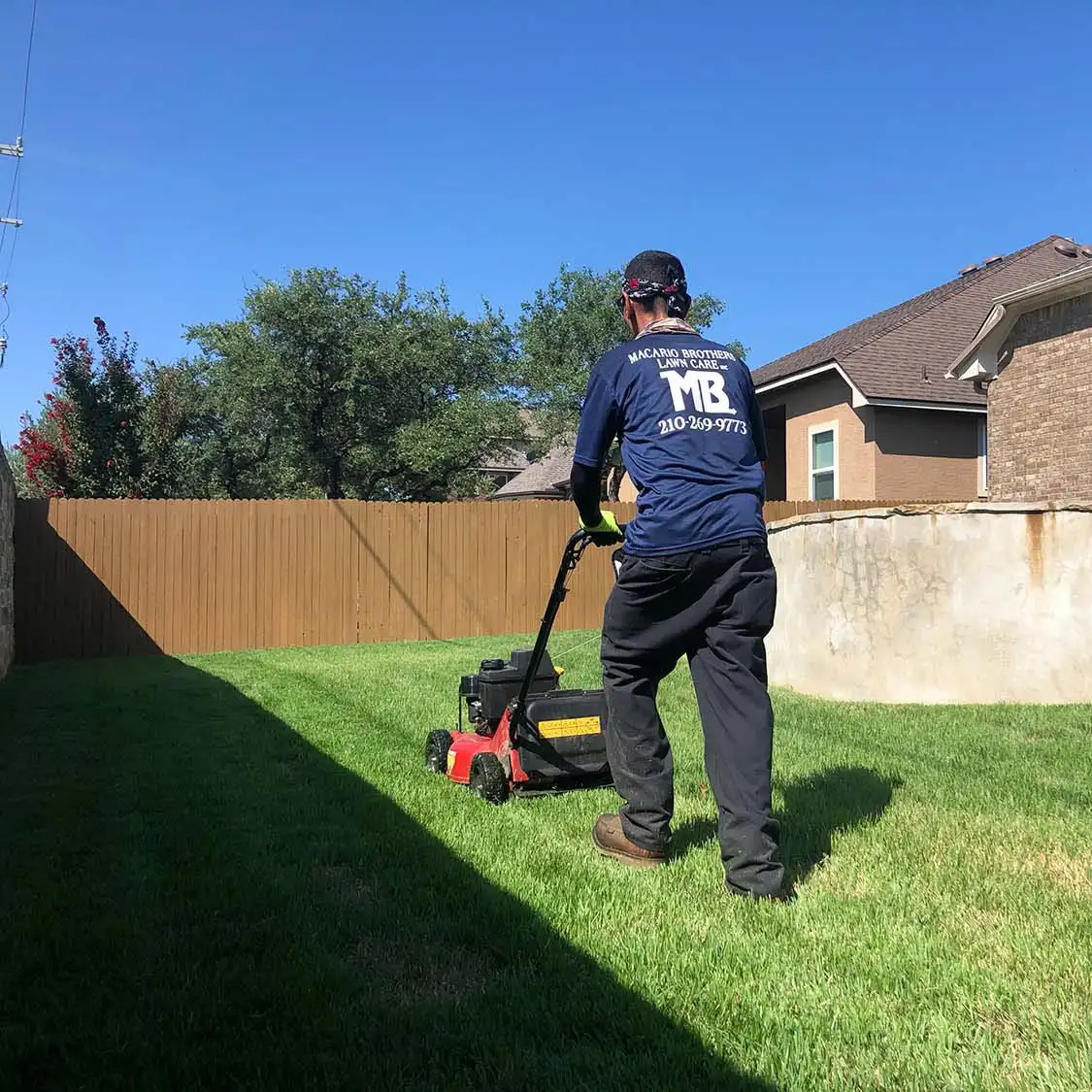 Macario Brothers Lawn Care crew member mowing a fenced San Antonio backyard lawn