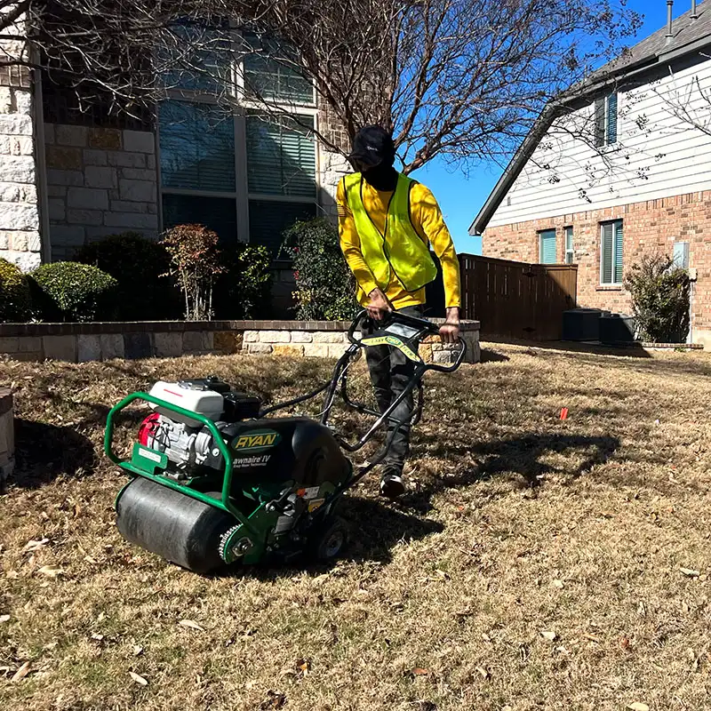 Lawn care technician core aerating a dormant front yard with Ryan Lawnaire IV