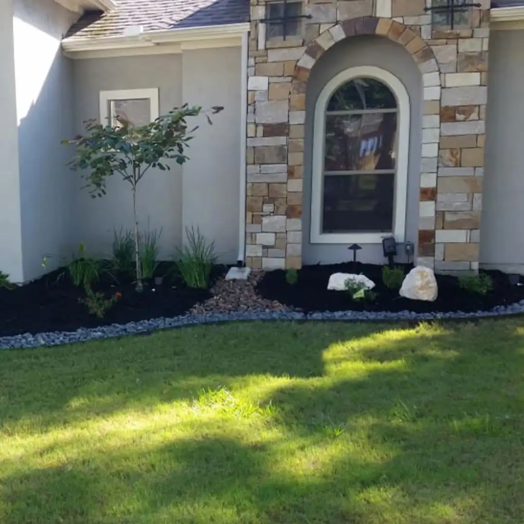 Fresh black mulch bed with stone border and new plantings along a San Antonio home